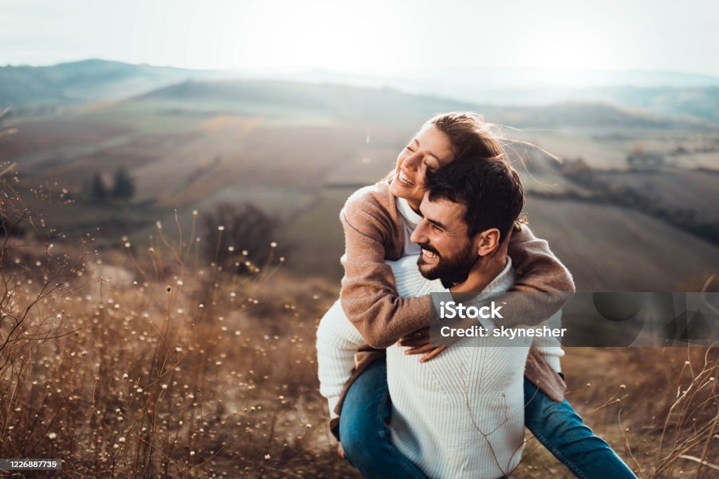 Young happy couple having fun while piggybacking on a hill.